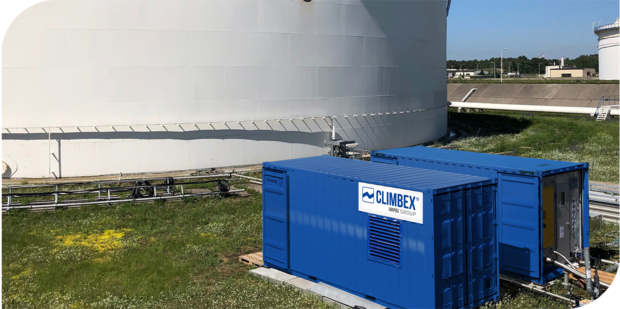 Das Bild zeigt ein Stück eines Tanks, oben im Bild, mit diversen LKWs und Anhängern davor, unten im Bild. Die Ladeflächen der zwei LKWs unten links im Bild, sind zu besseren grafischen Darstellung, geöffnet und zeigen eine Art Filtersystem welches mit einem Schlauch zum Tank verbunden ist.