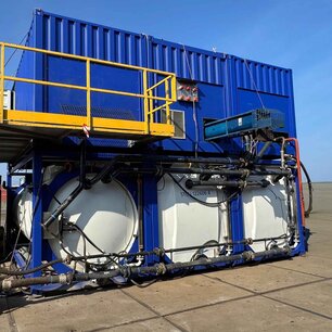 Zu sehen ist eine Konstruktion auf einem Gelände, bestehend aus drei großen weißen Tanks auf denen jeweils ein königsblauer Container steht in dem vermutlich die Motoren und Rohre sind.