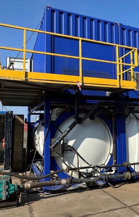 Zu sehen ist eine Konstruktion auf einem Gelände, bestehend aus drei großen weißen Tanks auf denen jeweils ein königsblauer Container steht in dem vermutlich die Motoren und Rohre sind.