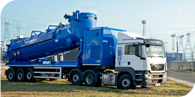 Das Bild zeigt ein Industriekühl- oder Kraftwerk. Im Zentrum des Bildes ragt ein massiver, zylinderförmiger Aufbau mit vielen Plattformen, Rohren und Leitungen in die Höhe, umgeben von der gewölbten Innenwand eines riesigen Kühlturms. Der untere Bereich ist in warmes orangefarbenes Licht getaucht, das von einer überdachten Konstruktion stammt, unter der zahlreiche Rohre, Ventile und Maschinen verlaufen.